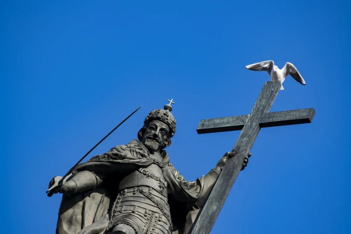 Statue holding a cross with a seagull against a blue sky